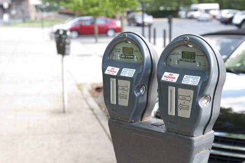On-street parking meter with cars bay parked in the background
