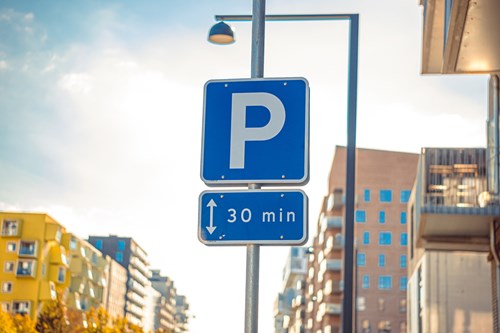 A blue parking sign displaying a 30 minute time limit, apartment buildings in the background