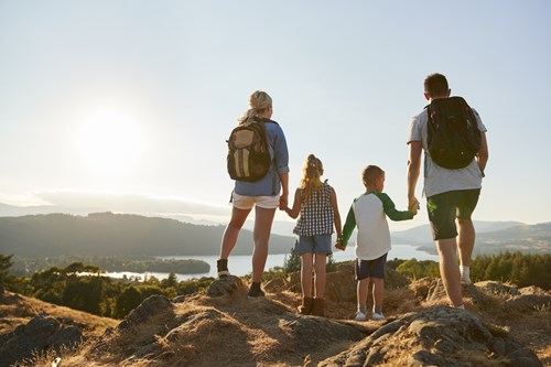 Woman, man and two children in hiking clothes hold hands as they look out at a mountainous view