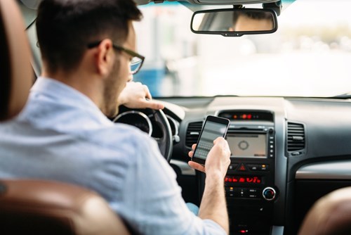 Parking apps, with their promise of contactless parking, are still proving popular with drivers. Man in a shirt at the wheel of a car looks at his mobile phone