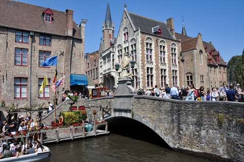 Stone bridge in Bruges full of tourists and tourists queuing for and getting into a boat