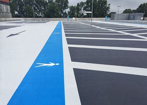Parking garage roof with gray waterproof surface, clearly marked bays and a blue pedestrian path