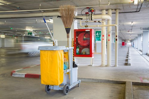 A cleaning cart with yellow bin bag and broom in a parking garage