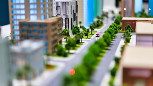 Miniature city showing red car moving along tree-lined avenue with skyscrapers either side