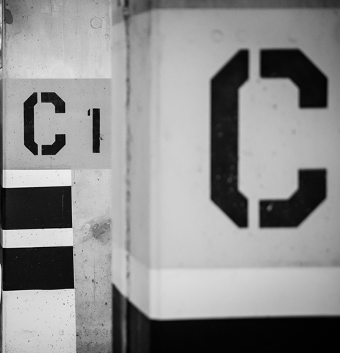 Grey pillars in a parking garage, stenciled with the letter C.
