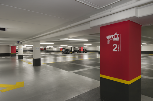 Bright parking garage with red columns and well marked dark grey parking bays