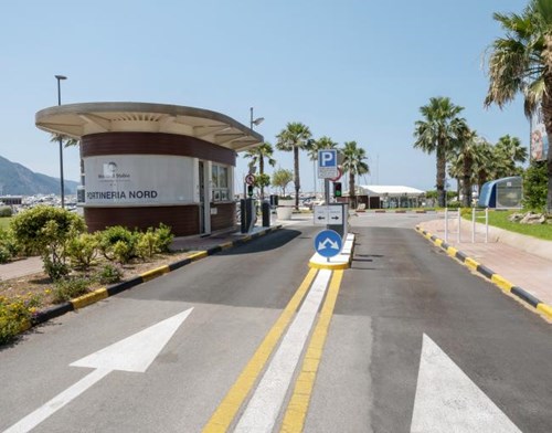 Entry and exit lane of an outdoor parking lot with a kiosk to the left and palm trees and mountain views in background