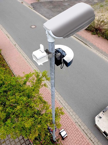 A battery operated sensor mounted on a lamppost above a parking lot