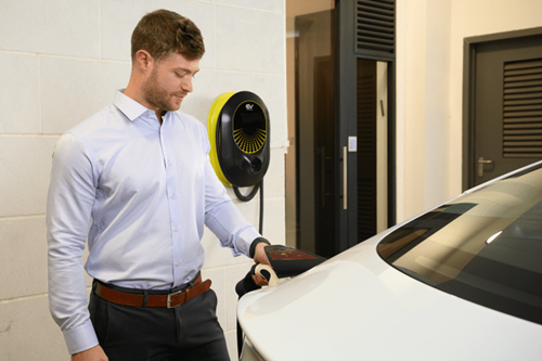 Man in business attire uses a wall-box EV charger on his white car