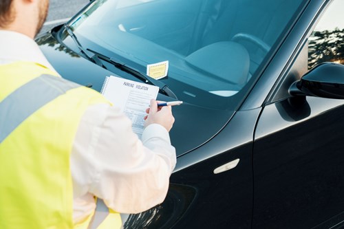 Enforcement officer in high-vis jacket leaves a parking notice on a windshield