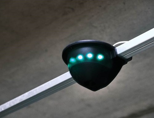 Parking sensor with green LEDs hangs from a parking garage ceiling