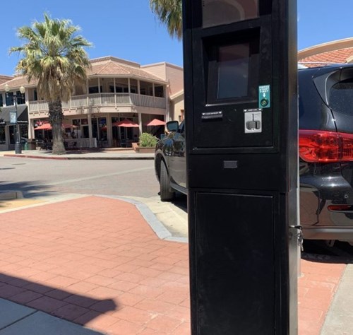 On-street parking meter with car in background and palm trees