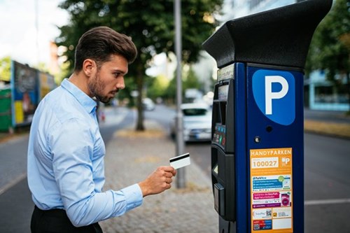 Businessman in blue shirt holds parking ticket up to an on-street parking meter