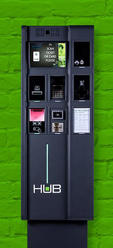 Parking pay stations with a green painted brick wall behind.