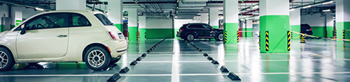 Interior of a parking garage with green painted columns and cars parked in a few of the bays