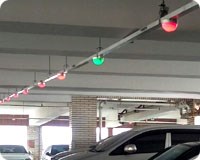 Parking garage with cars parked beneath the red and green lights of a PGS system
