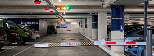 Interior of a parking garage showing a lane, line of columns and bays in parked cars.