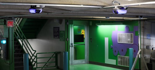 Stairwell of a parking garage decorated with green wall and blue train. Blue parking guidance cameras suspended from the ceiling.