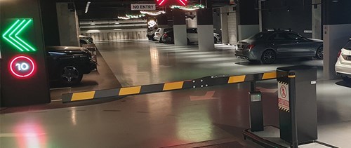 Yellow and black parking barrier in an indoor parking facility with cars parked in bays and a green chevron light on wall