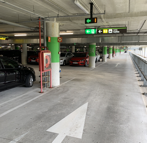 Interior of a parking garage showing concrete columns with a green stripe, green parking guidance arrow and fire escape sign