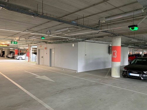 Interior of a parking garage showing concrete columns with red stripes and green parking guidance sensors