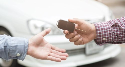A man in a checkered shirt hands a car key to a man in a grey shirt