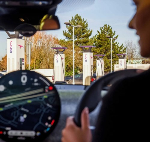 Driver views Ionity EV chargers through windshield while navigating car display.
