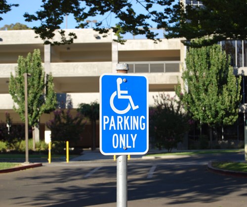 A disabled parking sign with a parking garage and trees in the background
