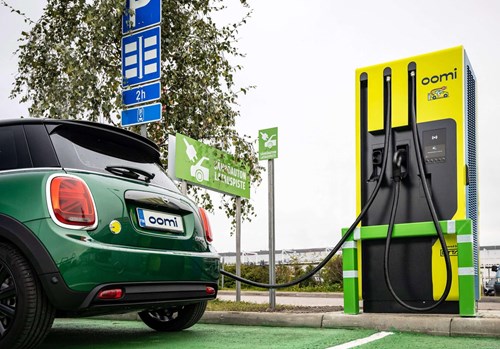 A green mini is parked in a green on-street parking pay, using a yellow EV charger branded with the Oomi logo.