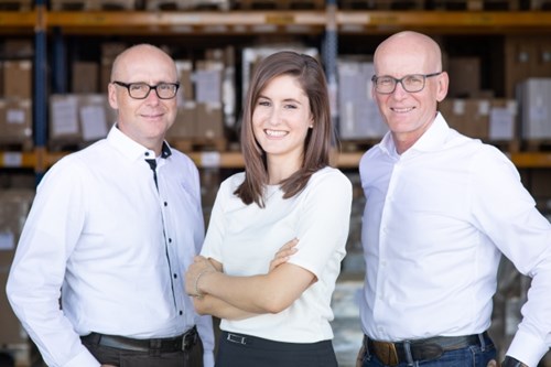 A business woman stands between two business men with warehouse in background