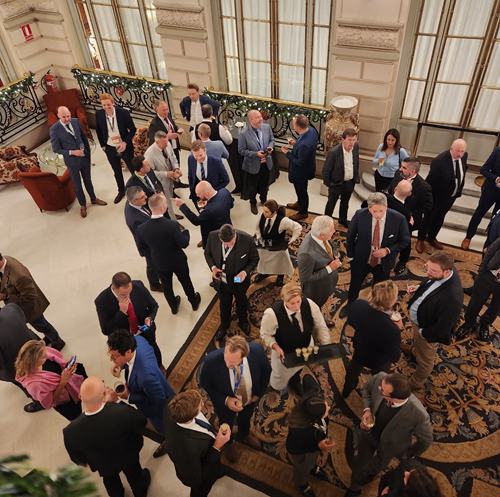 Business men and women stand in an opulent room networking over drinks and canapes