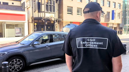 CEO Civil enforcement officer standing next to a parked car.