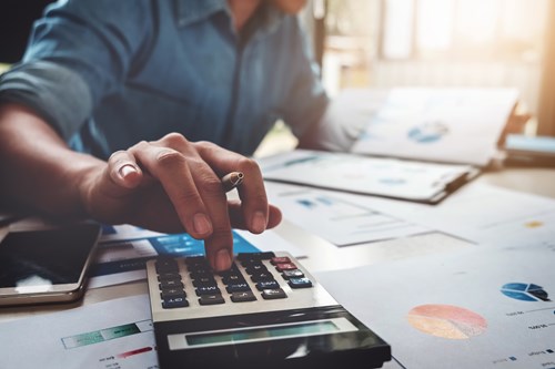 Maintaining revenue and meeting budgets is a big hurdle to overcome. Man at a desk uses calculator and looks at papers filled with graphs